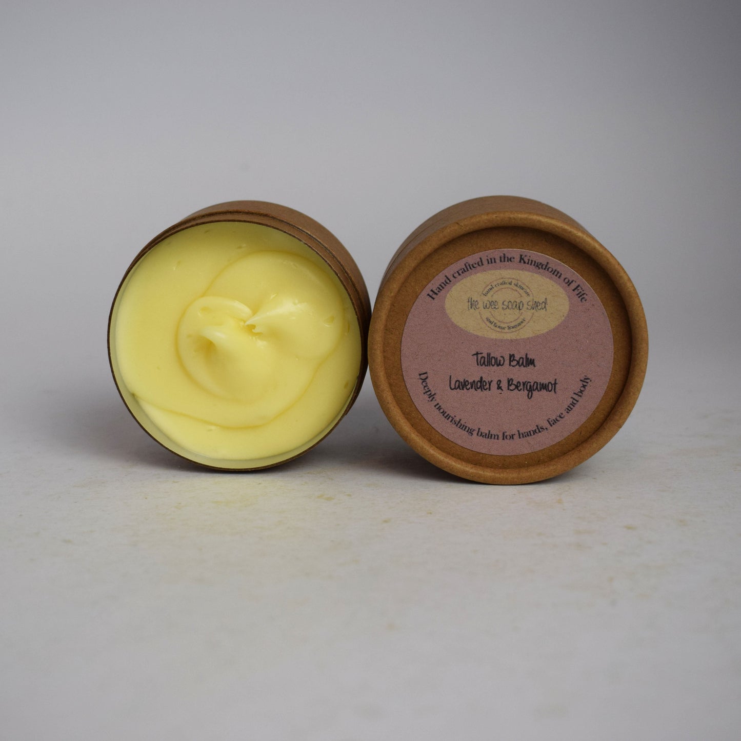 Creamy tallow balm in cardboard container with white background
