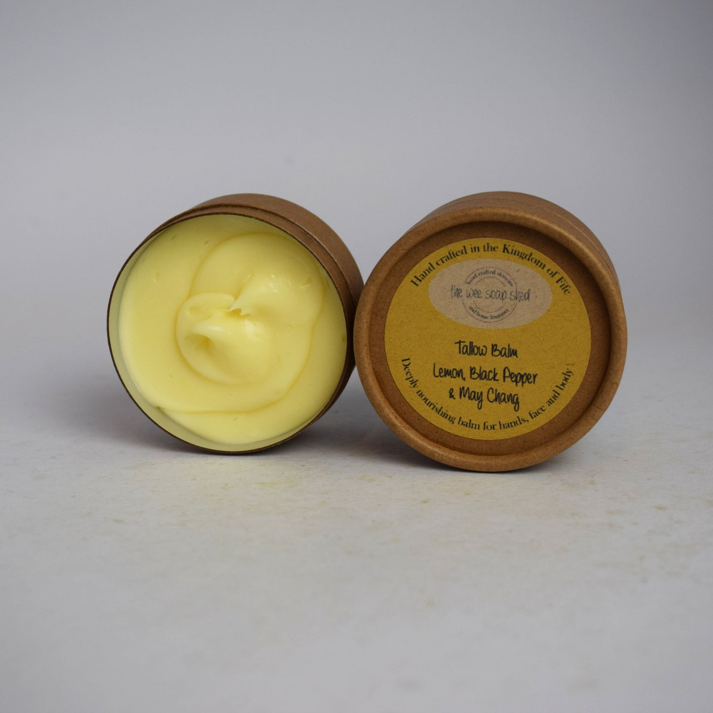 Two cardboard containers, one without lid showing creamy yellow tallow balm on  a white background