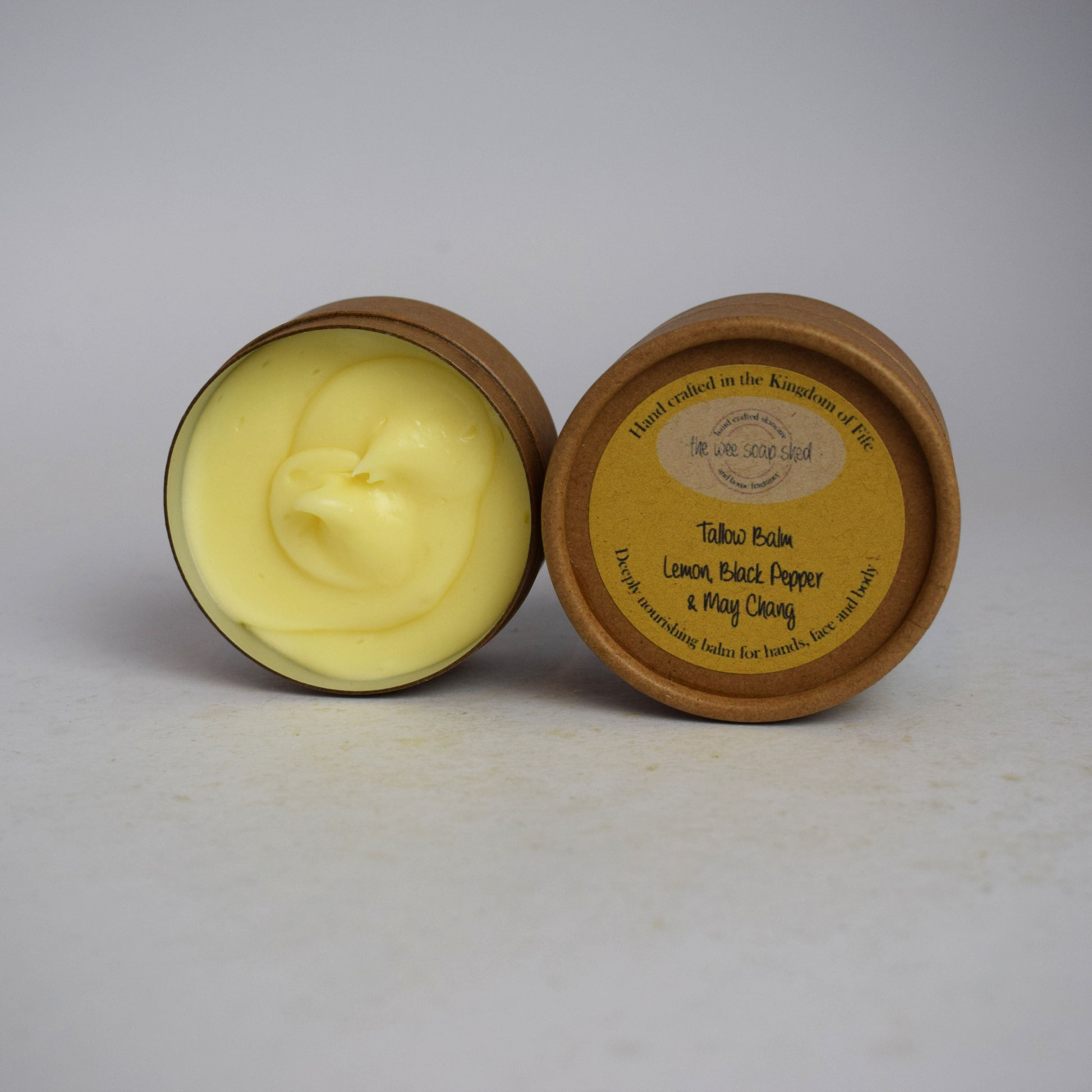 Two cardboard containers, one without lid showing creamy yellow tallow balm on  a white background