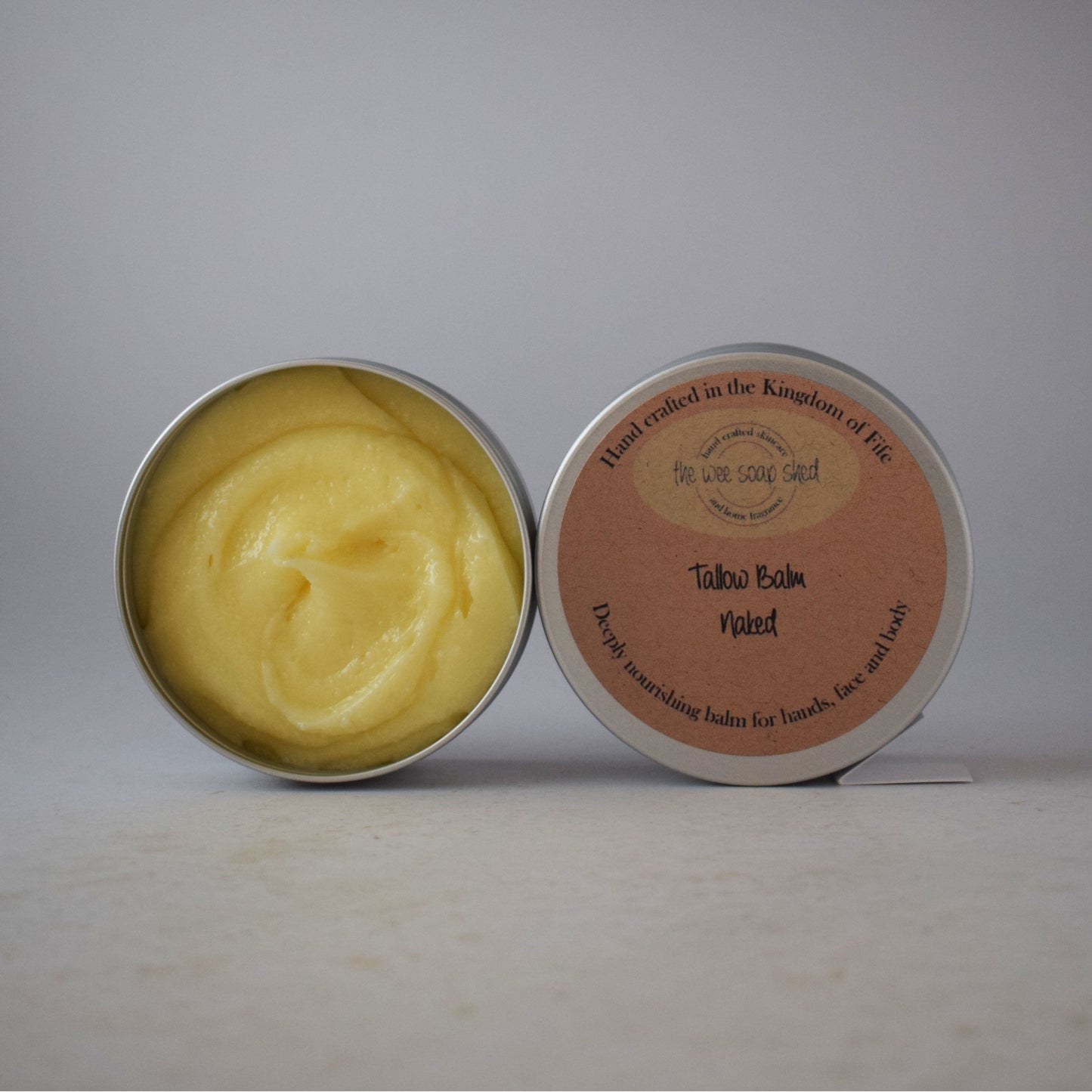 Open tin of yellow balm with a pink label on a gray background