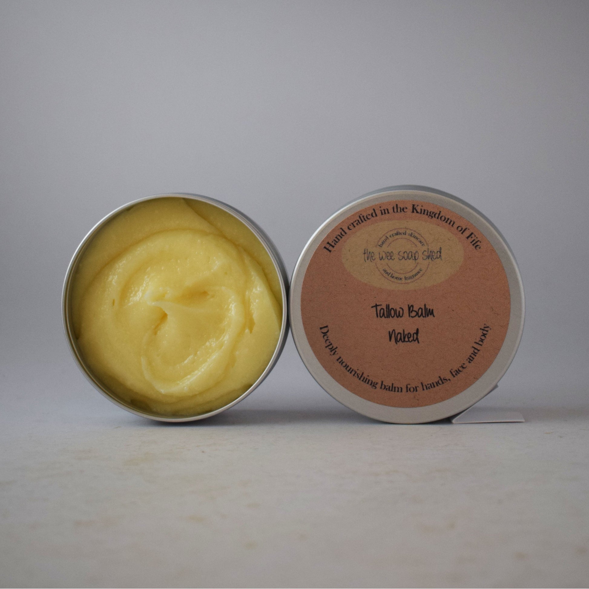 Open tin of yellow balm with a pink label on a gray background