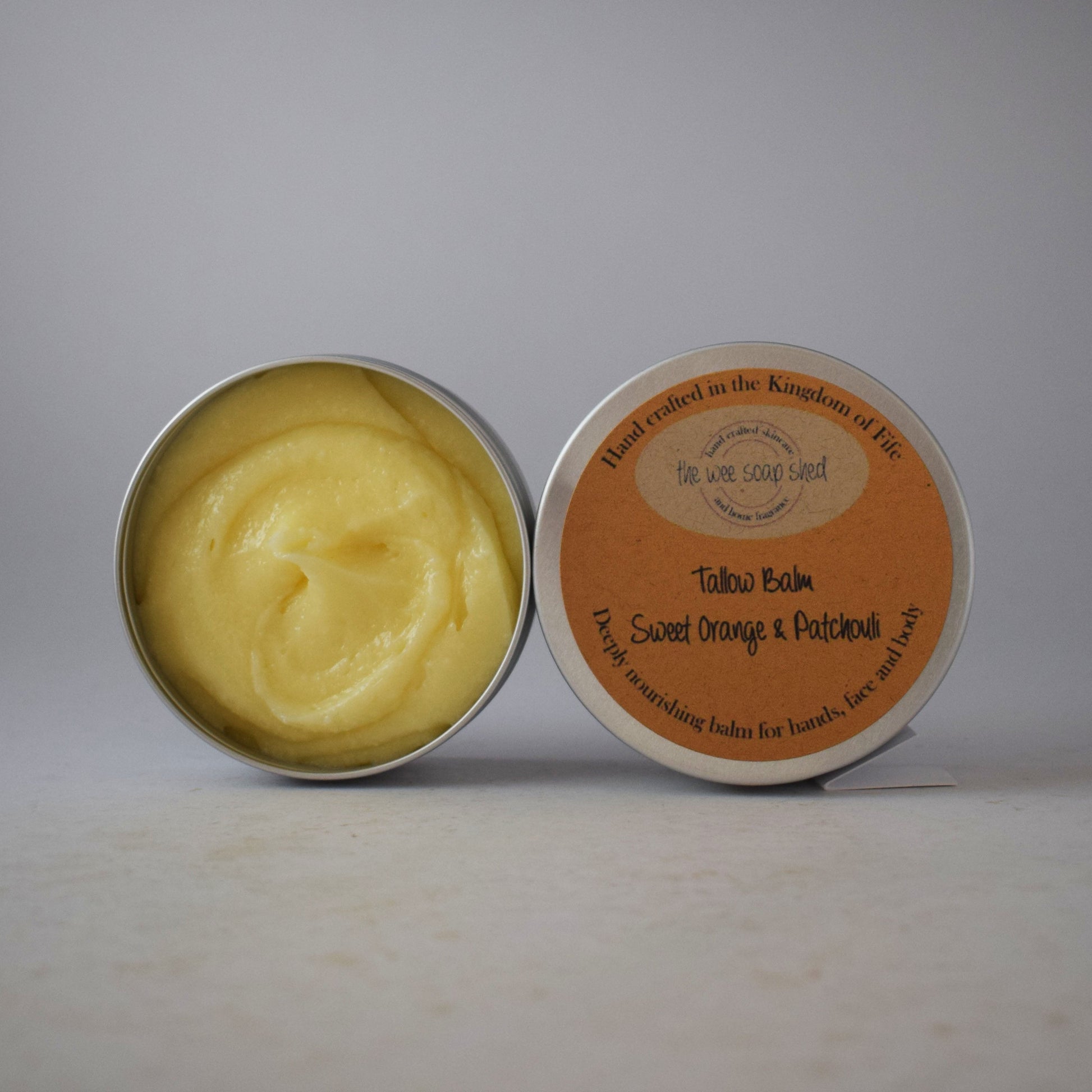 Open tin of yellow balm with orange label on a gray background