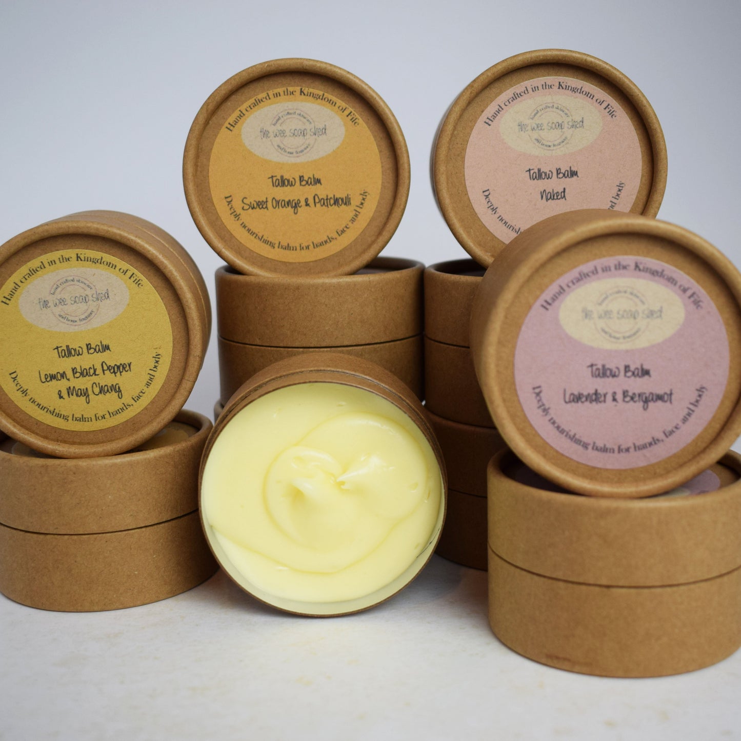 Collection of round cardboard containers with some open showing yellow creamy tallow balm