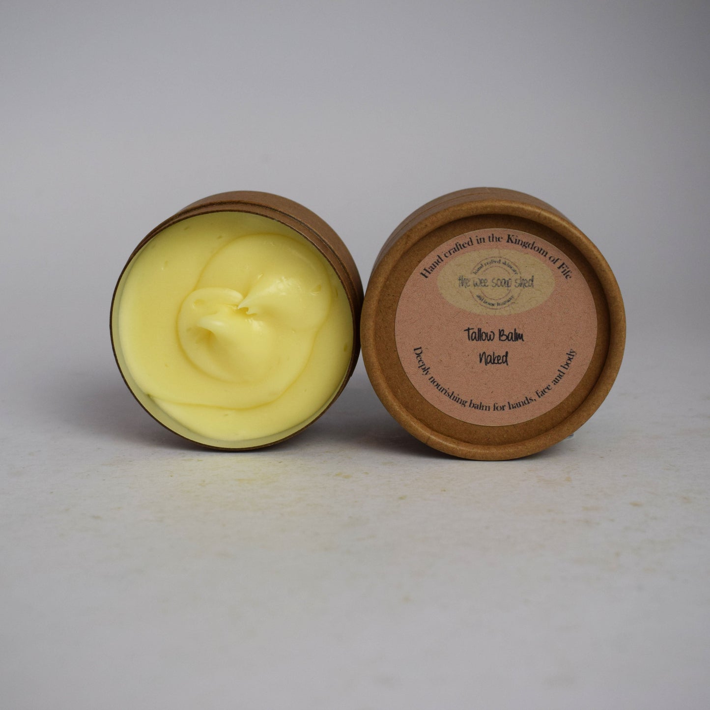 Two cardboard containers, one without lid showing creamy yellow tallow balm on white background