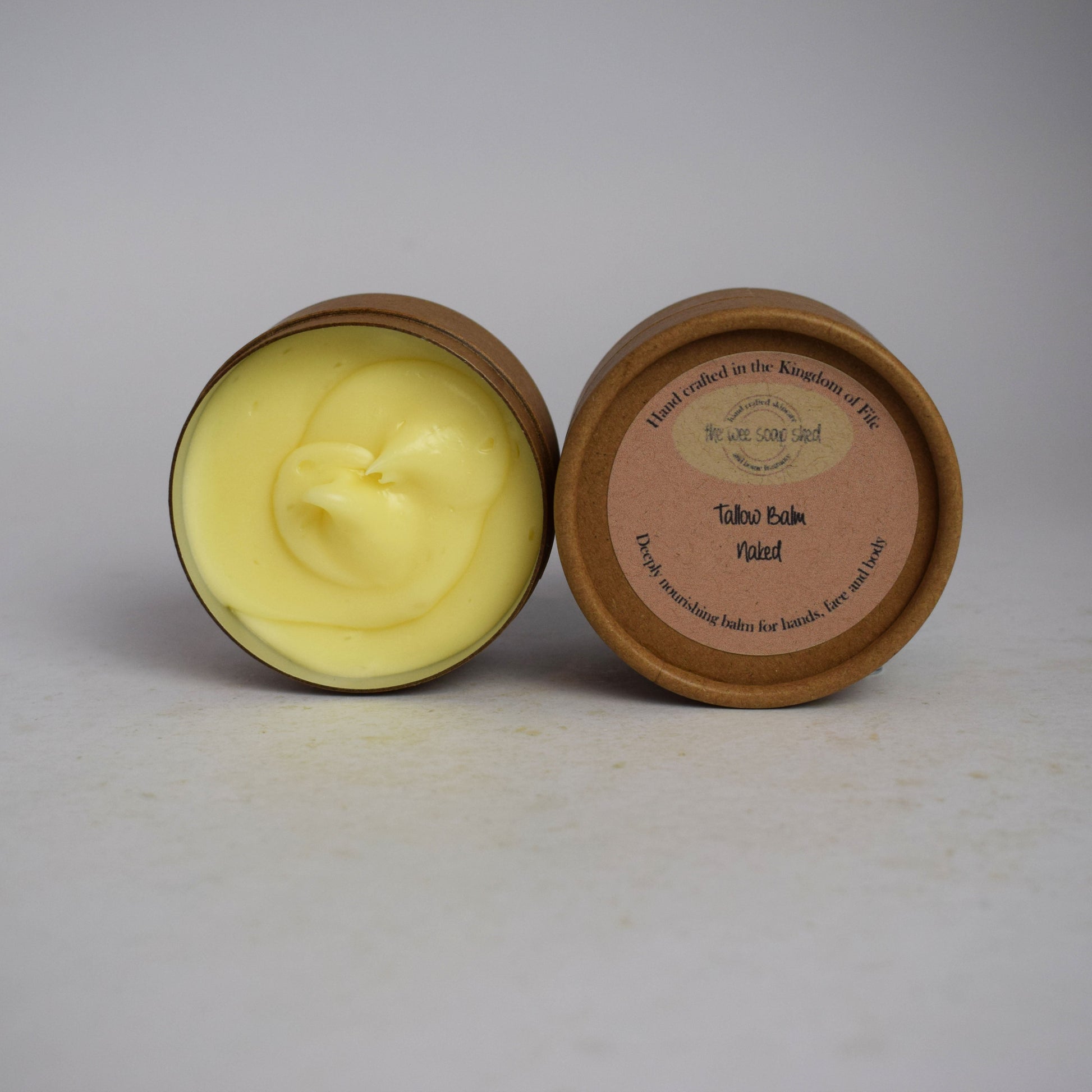 Two cardboard containers, one without lid showing creamy yellow tallow balm on white background