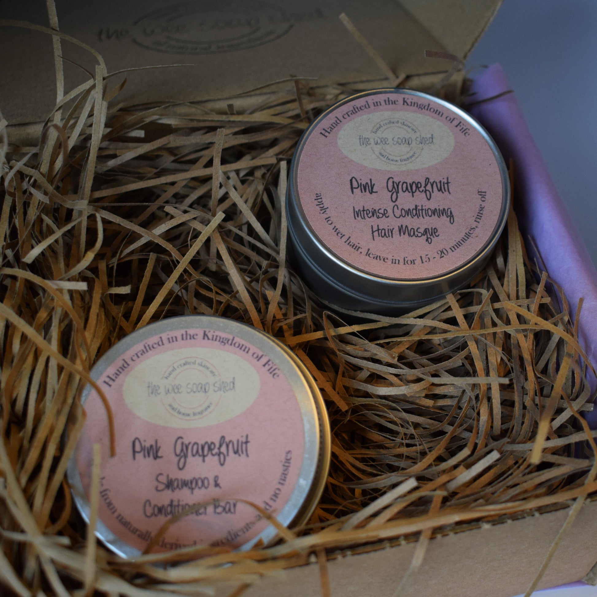 Two tins of 'Pink Grapefruit' products in a box with straw bedding.