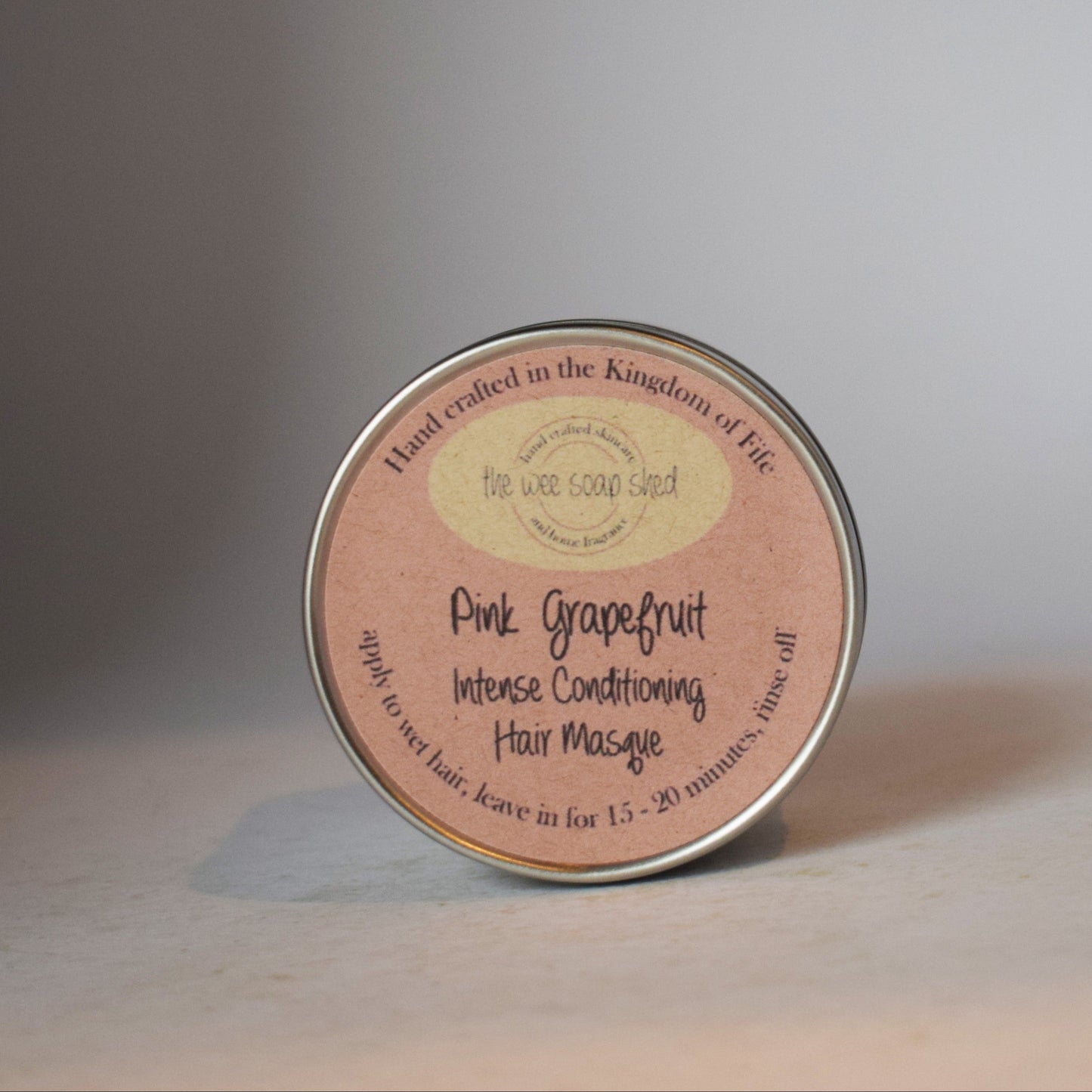 Pink grapefruit hair massage product container on a neutral background