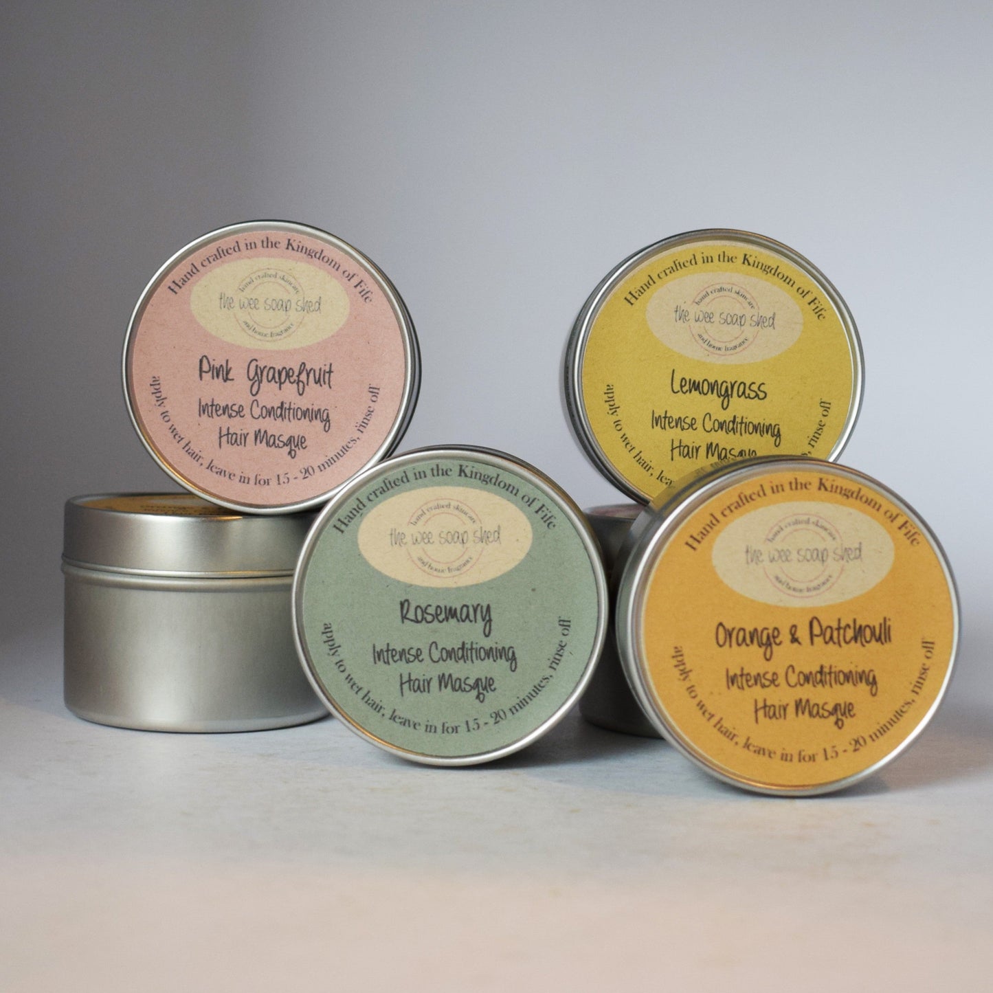 Five tins of hair massage with colorful labels on a gray background