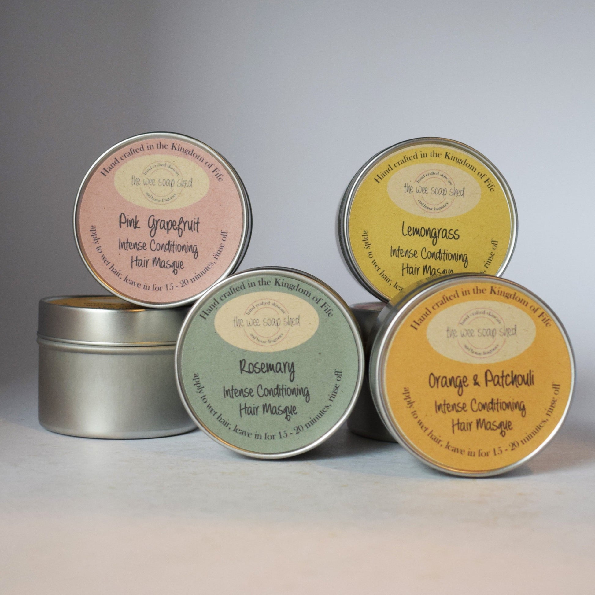 Five tins of hair massage with colorful labels on a gray background