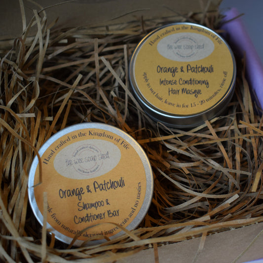 Two tins of 'Orange & Patchouli' products in a box with straw-like material.
